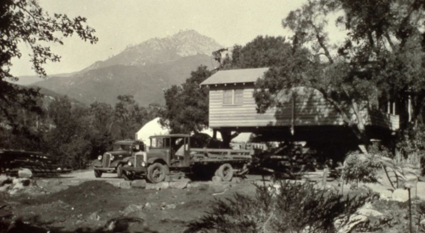 duplicate of SBBG_PR_02742, Moving the Cottage building, with greenhouse in background