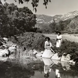 Two young women enjoy their own reflections in a quiet pool with a background of sand strawberries in bloom and mountains rising above