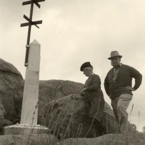 Black and white photograph of two people standing to the right of a monument on large rocks.