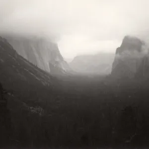 Black and white photograph of mountain range with fog covering mountain tops.